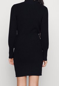 Abito nero a coste con maniche lunghe e collo alto, caratterizzato da una silhouette aderente e un orlo che arriva a metà coscia.