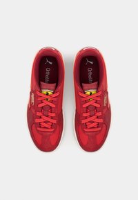 Chaussures de sport rouges avec une combinaison de textures lisses et en daim, dotées de lacets, de semelles en caoutchouc et d'un accent de logo sur le côté.