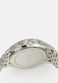 Orologio in acciaio inossidabile con cassa lucidata, cinturino a maglia in tono argento e due pulsanti di comando. Il retro presenta un logo inciso e il grado di impermeabilità.