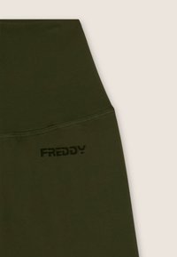 Leggings highwaist verde oliva con una texture liscia e un logo "FREDDY" nero sulla vita. Design senza cuciture con tessuto elasticizzato.