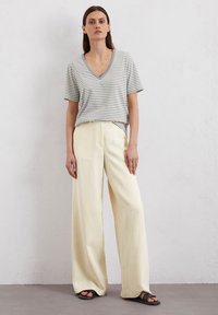 Striped gray and white v-neck t-shirt, loose fit, paired with cream wide-leg pants and black slide sandals. Smooth, breathable fabric texture.
