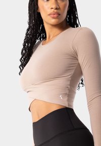 Bežs garām piedurknēm tops ar savītu priekšpusi, kombinēts ar augstākā jostasvietā melnajām legingām. Mīksts, elastīgs audums ar smalkiem šuvju detaļām.