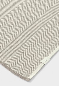 Vævet stof i beige og hvidt fiskebensmønster, der har en struktureret finish og et lille mærket label på kanten.