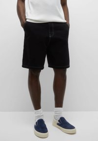 Short en jean noir avec coutures claires, poches latérales. Associé à des chaussures bateau bleu marine et des chaussettes blanches. Design simple, coupe contemporaine.