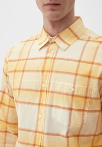 Gelb-orange kariertes Hemd aus leichtem Material. Verfügt über eine Knopfleiste, einen spitzen Kragen und eine einzelne Brusttasche.