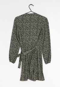 Langärmliges Wickelkleid in olivgrün mit schwarzem Punktenmuster, mit Tunnellinie in der Taille und Rüsche am Saum. Aus leichtem Stoff gefertigt.