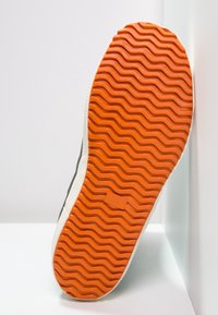 Suela de zapatilla con un patrón ondulado naranja y bordes blancos. Talla marcada como 39. Superficie texturizada para agarre. Diseño simple y funcional.