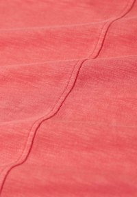 Korallfärgad tyg med mjuk textur, som har subtila variationer i väv och en kurvad sömdetalj som löper genom materialet.