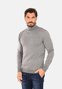 Maglione grigio a collo alto realizzato in morbido tessuto a maglia, con un design aderente e polsini e orlo a coste, abbinato a jeans blu scuro.