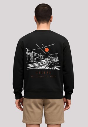 Schwarzer Sweatshirt mit einem Grafik auf der Rückseite, die eine stilisierte Landschaft, Linien und eine rote Sonne zeigt, mit dem Text "FLIEH UND ENTDECKE DIE WELT."