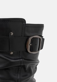 Czarna skórzana botka o zmiętej konstrukcji, z szerokim mankietem, paskiem z klamrą w kolorze srebrnym oraz kontrastującymi detalami szycia.