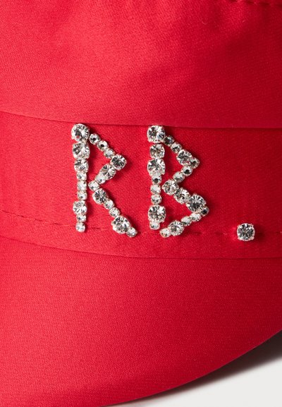 Tissu rouge avec les lettres KB et un point formé de petits strass ronds transparents cousus à la surface.