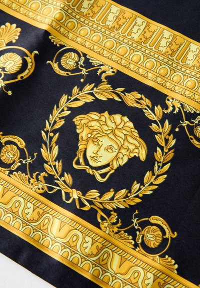 Jedwabny szalik z czarnym tłem ozdobiony misternymi złotymi wzorami, w tym centralnym medalionem z twarzą i dekoracyjnymi obramowaniami.
