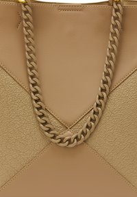 Beige bőr kézitáska texturált felülettel, háromszög alakú dizájnnal és vastag lánc pánttal. Figyelemre méltó varrás emeli ki a struktúrát.