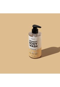 Gjennomsiktig plast pumpeflaske med Breakout Body Wash for sensitiv hud på beige bakgrunn med skygge.