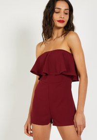 Mono sin tirantes burdeos con un volante, cuerpo ajustado y pantalones cortos. Tela suave y elástica con costuras limpias y sin herrajes visibles.
