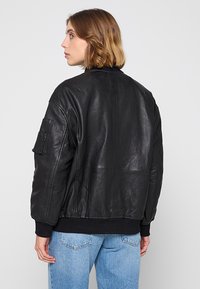 Svart läderbomberjacka med ribbad nederkant, synliga sömmar och en sidoficka. Bärs med ljusblå denimjeans.