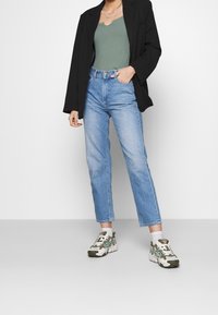 Sort blazer, grøn ribbet top, lyseblå høj talje lige jeans og grønne og hvide sneakers med strukturerede mønsterdetaljer.