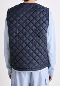 Marineblaue gesteppte Steppweste mit Diamantmuster, aus synthetischem Material; verfügt über einen runden Ausschnitt und offene Armlöcher.