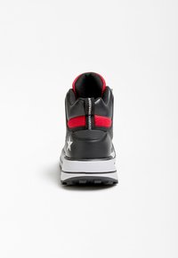 Musta ja punainen urheilukenkä, jossa on teksturoitu päällinen, valkoinen tähden korostus ja paksu valkoinen pohja, varustettu vetoketjullisella takaosalla.