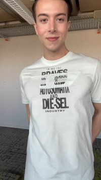 Jeune homme souriant à l'intérieur portant un t-shirt blanc avec un texte noir sur l'industrie automobile et le diesel.