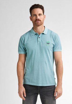 Polo bleu clair en coton avec une patte de boutonnage à trois boutons, des manches courtes et un écusson logo vert sur la poitrine gauche.