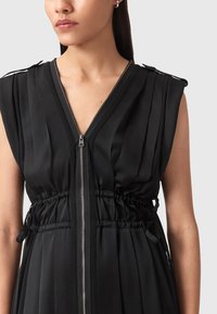 Vestito nero senza maniche con pieghe verticali, scollatura a V, vita con cordoncino regolabile e chiusura frontale con zip. Tessuto dalla texture liscia.