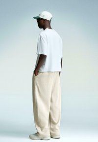 White short-sleeve t-shirt, beige ribbed wide-leg pants, and a light cap. The design features pockets, a relaxed fit, and textured fabric.