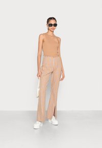 Top assimétrico laranja combinado com calças de cintura alta em padrão xadrez nas cores laranja e branco. As calças possuem fendas nos tornozelos. Usadas com sapatilhas de plataforma.