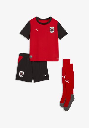 Rød og sort kortærmet fodboldtrøje med logoer, sorte shorts med røde detaljer og matchende røde knæstrømper med grå såler.