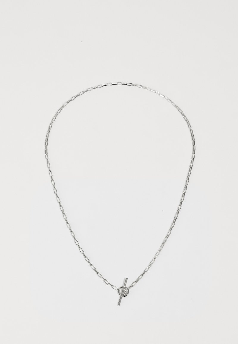 Az ezüst láncnyaklánc megnyújtott szemekből áll, fényes rúdzárral és kör alakú díszítéssel rendelkezik. A design minimalista és elegáns.