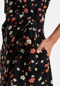Robe en tissu noir avec un motif floral comprenant des fleurs roses, oranges et blanches. Détail de taille nouée et poche latérale visible.