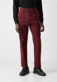 Chino en coton bourgogne avec une coupe droite, poches avant, fermeture à bouton et devant plat. Porté avec des chaussures de sport noires.