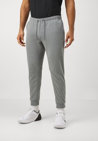 Gray sweatpants made of soft fabric, featuring a drawstring waist, tapered fit, and ribbed cuffs. Paired with white athletic shoes.