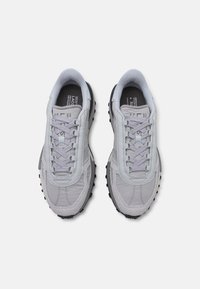 Gray athletic sneakers with a smooth upper, textured accents, tonal laces, and a black rugged sole for traction. Lightweight design.