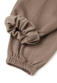 Bruine katoenen jogger met elastische boorden, voorzien van een gladde textuur en zichtbare stiksels. De stof lijkt zacht en warm.