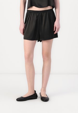 Black satin shorts with an elastic waistband, paired with black flat shoes. The shorts have a loose fit and smooth texture.