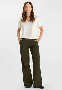 T-shirt léger à col en v couleur crème, associé à un pantalon taille haute à jambes larges de couleur vert olive, présenté en position debout sur un fond neutre.