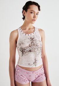 Top roz din bumbac cu accente metalice și un model floral, asociat cu pantaloni scurți roz cu nervuri, decorați cu butoane decorative de diverse dimensiuni.