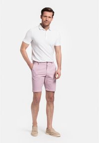 Witte polo met korte mouwen en een drieknoopsluiting; roze shorts met zijzakken en een knoopsluiting; beige instap schoenen.