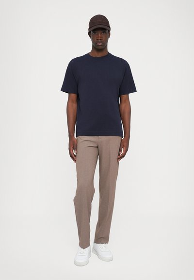 T-shirt en coton bleu marine, pantalon tailleur beige clair et baskets blanches. Look décontracté avec un design minimaliste et une casquette marron foncé.