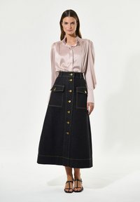 Seidenbluse in hellrosa mit Puffärmeln; Jeansrock in Dunkelblau mit goldfarbenen Komponenten, großen Taschen und vorderem Knopfverschluss.