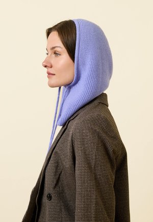 Gestrickte lavendelfarbene Balaclava mit Bändern, kombiniert mit einem braunen karierten Blazer. Glatte Textur und markante Form, die das Gesicht umschmeichelt.