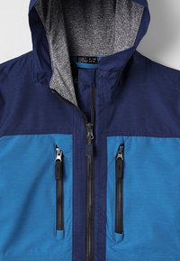 Chaqueta de cremallera en azul marino y azul con un forro interior gris, dos bolsillos frontales con cremallera y una capucha de tela texturizada.