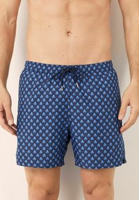 Bañador azul marino con un patrón repetido de pulpos en azul claro, cintura elástica con cordón, y tejido suave y ligero.