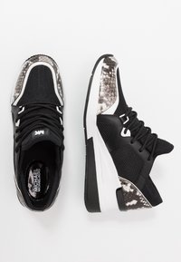 Zapatillas negras con parte superior de malla, acentos de estampado de serpiente y suelas de goma blanca. Presentan cordones negros y un collar acolchado para mayor soporte.