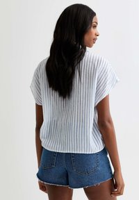 Camisa de manga corta a rayas en tejido azul claro y blanco, con un corte relajado. Combinada con pantalones cortos de denim, que presentan acabados deshilachados.