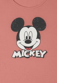Cara sonriente de Mickey Mouse estilo vintage con orejas y nariz negras sobre la palabra "MICKEY" en un fondo de tela rosa.