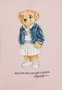 Illustration av en björn som bär en jeansjacka, vit klänning med volanger och vita sneakers. Bakgrunden är ljusrosa. Har logotyptext nedanför.