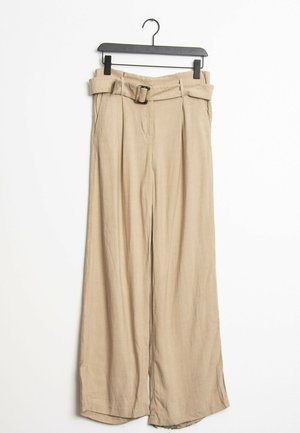Pantalones de pierna ancha beige con cintura alta, que incluyen un cinturón de tela, pliegues y una textura ligera, colgando de una percha negra.